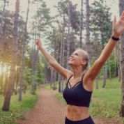 Joggerin in schwarzem Fitness-Dress blickt in Kiefernwäldchen nach oben und streckt ihre Arme zum Himmel Joggerin in schwarzem Fitness-Dress blickt in Kiefernwäldchen nach oben und streckt ihre Arme zum Himmel